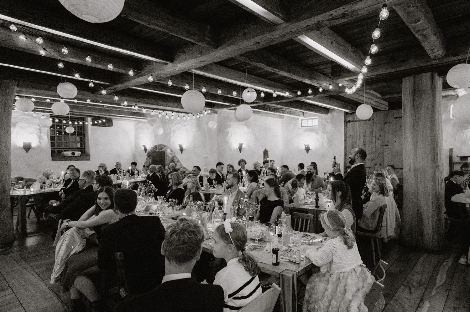 Wide angle view of a reception hall filled with guests and string lights.