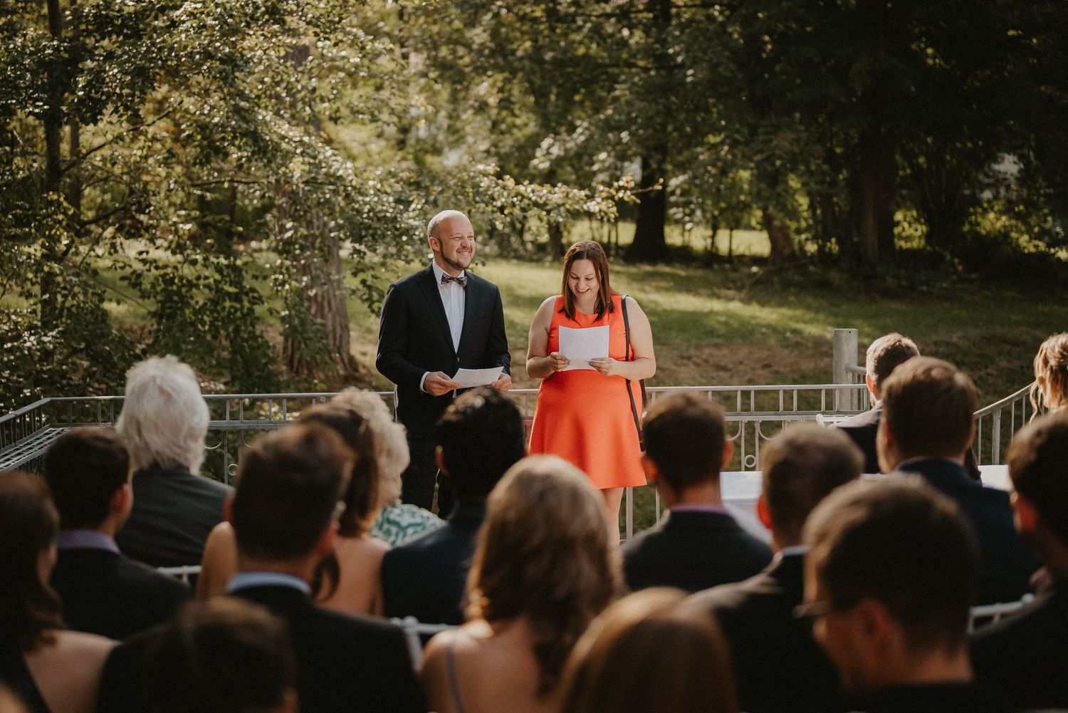 Wedding ceremony guests watching proceedings from rows of white chairs at outdoor venue.
