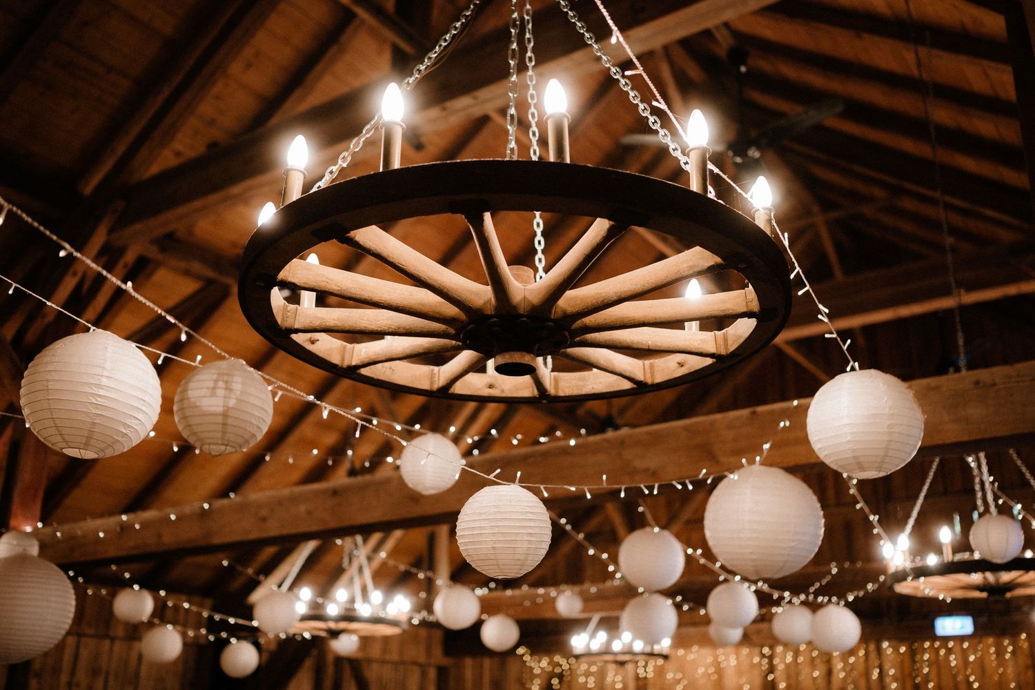 Wooden beamed ceiling decorated with string lights and white paper lanterns creating a warm ambiance.