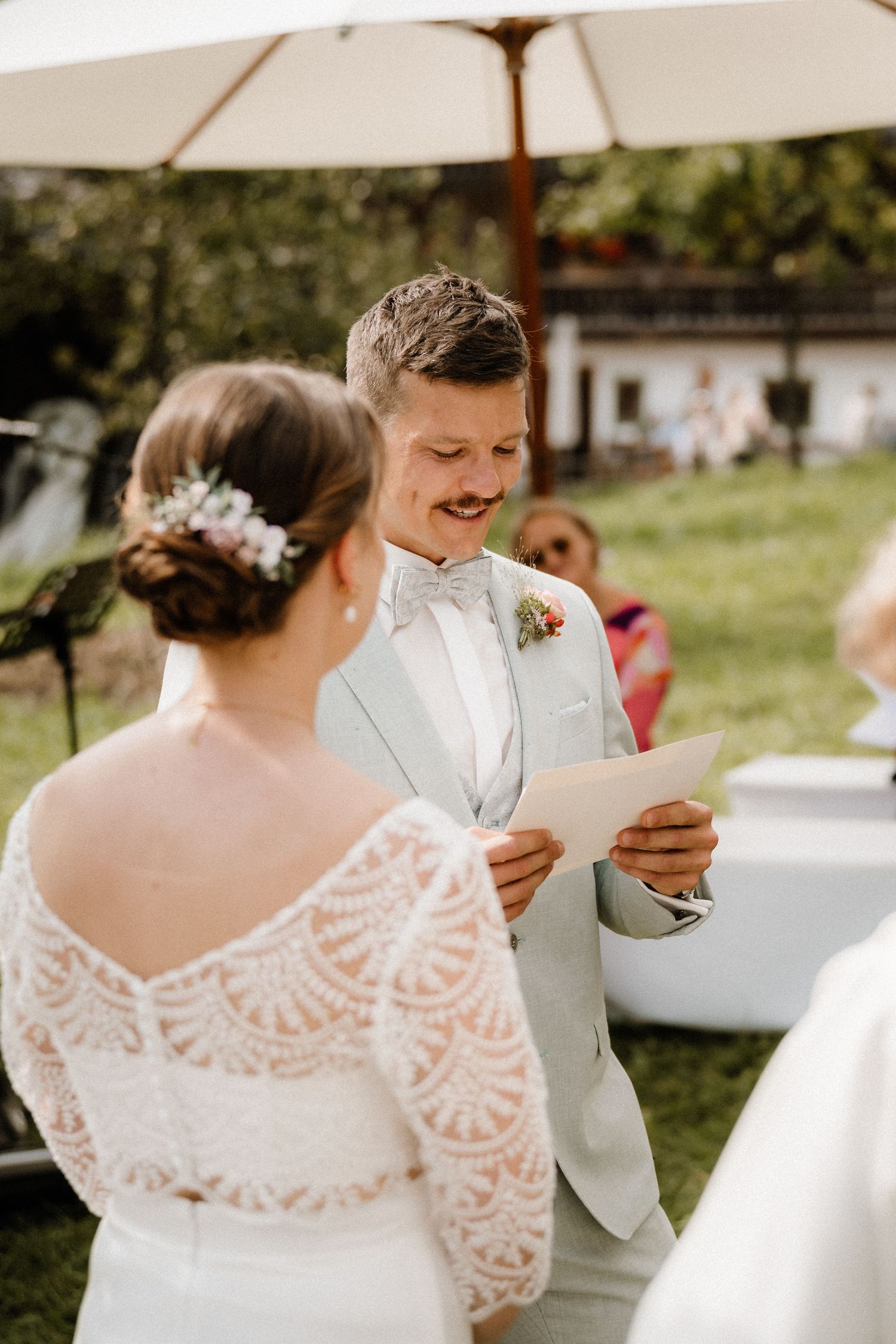 Intimate outdoor wedding ceremony moment with lace dress and light gray suit.