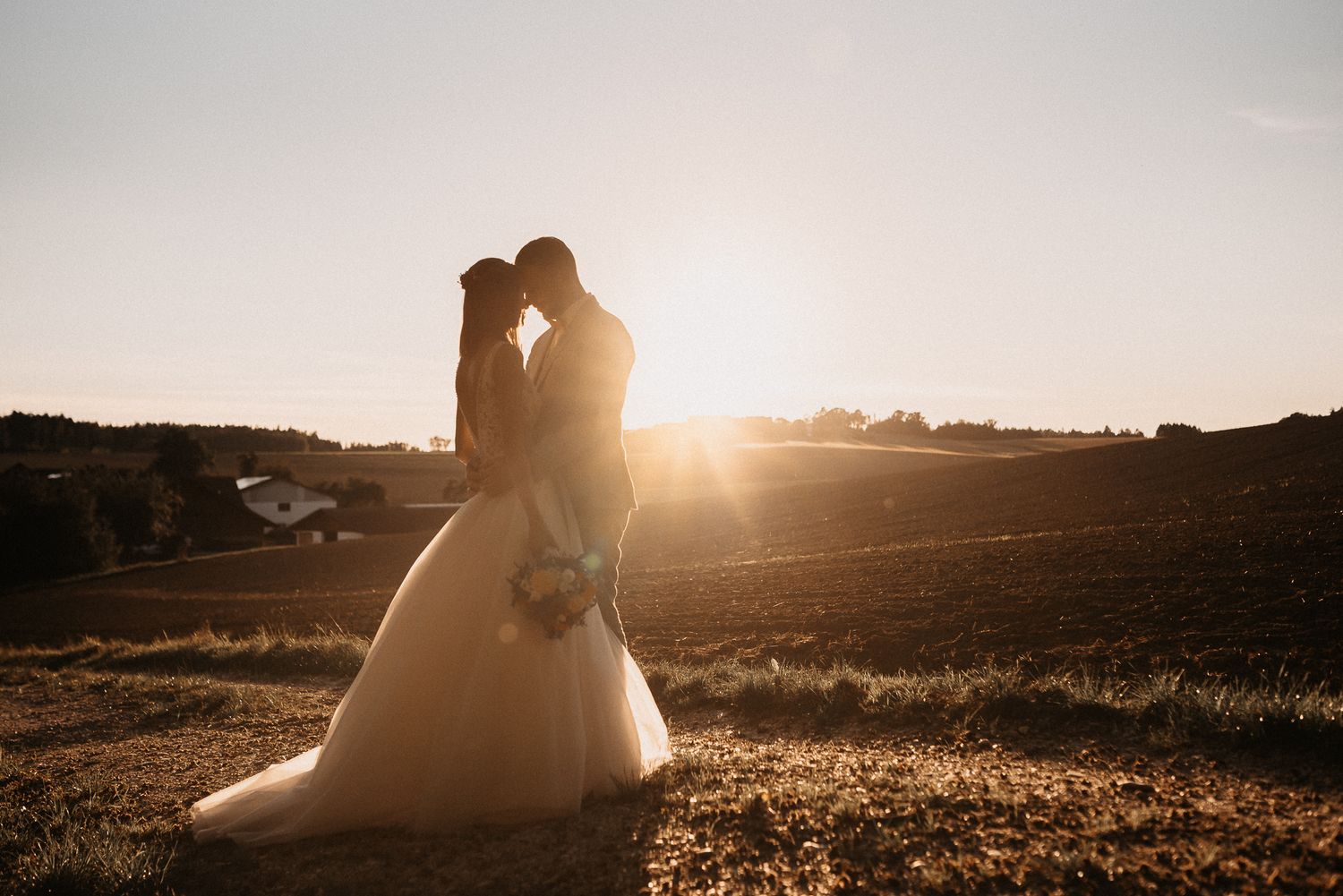 Silhouettenpaar, das sich im goldenen Sonnenuntergangslicht über die romantische Landschaft umarmt. Von Dama Fotografie Bad Tölz