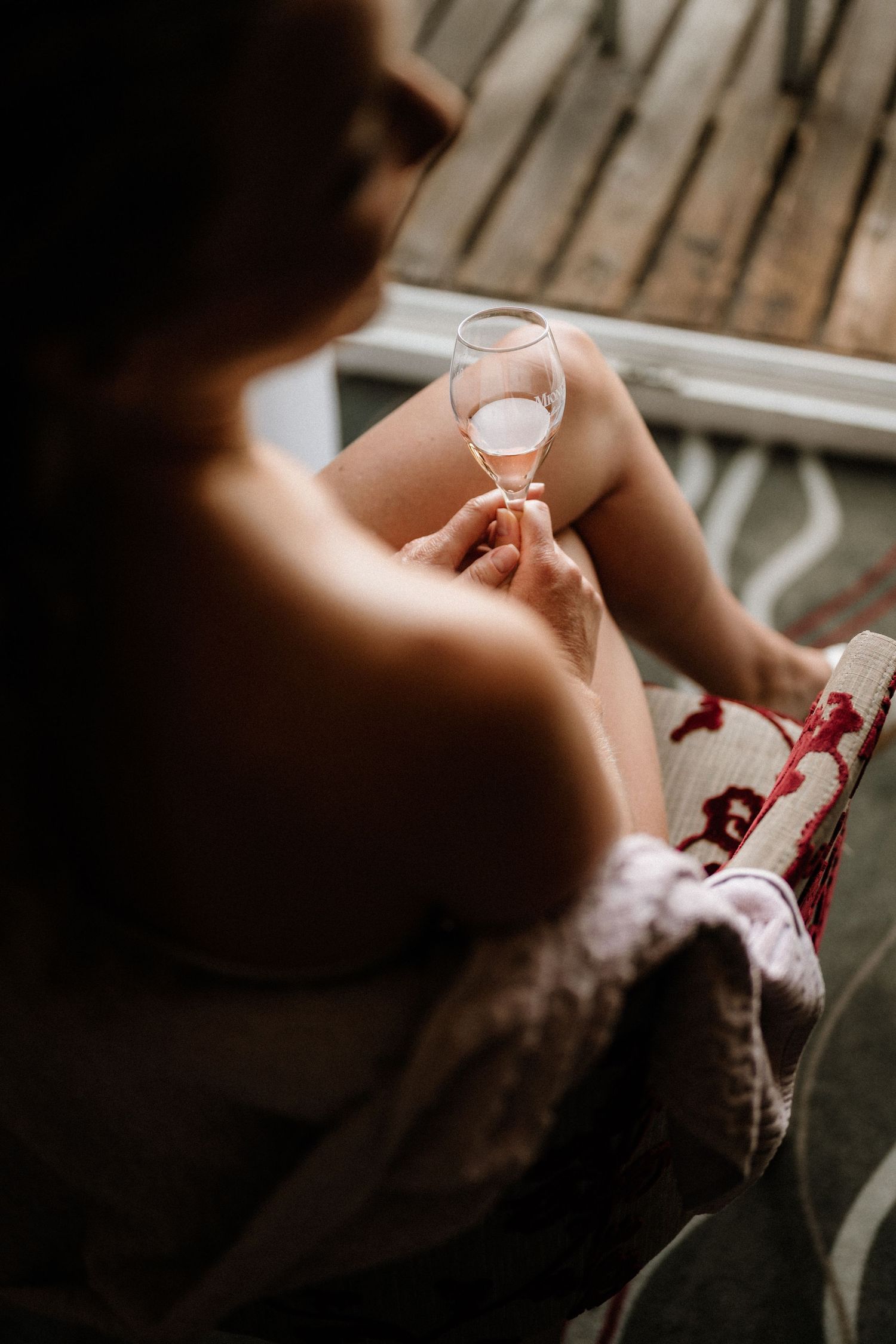 Person holding wine glass while sitting on wooden deck outdoors.