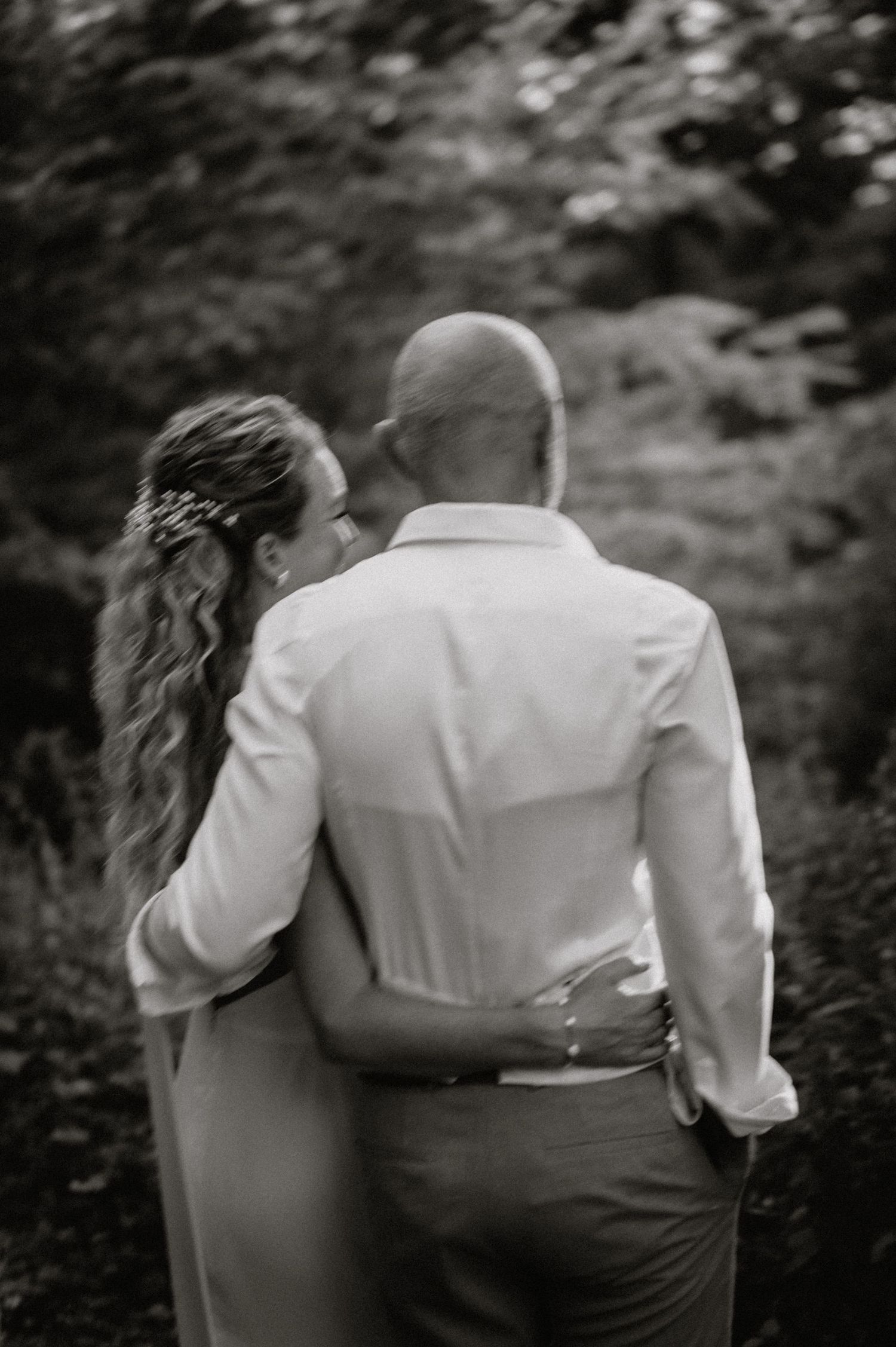 A black and white portrait captures a couple from behind in formal wedding attire.