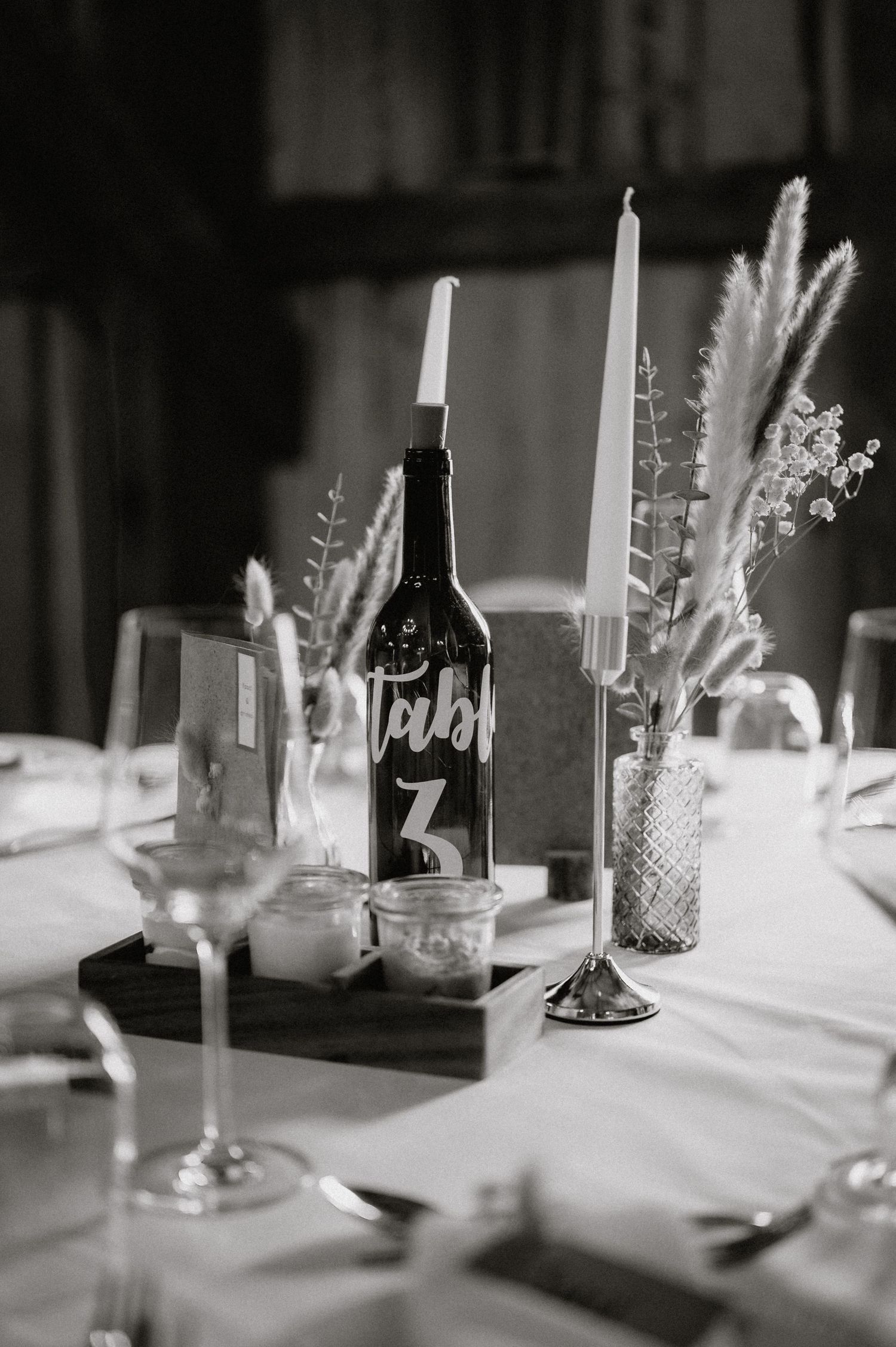 Black and white photo of wedding table decorations with candles and wine bottles.