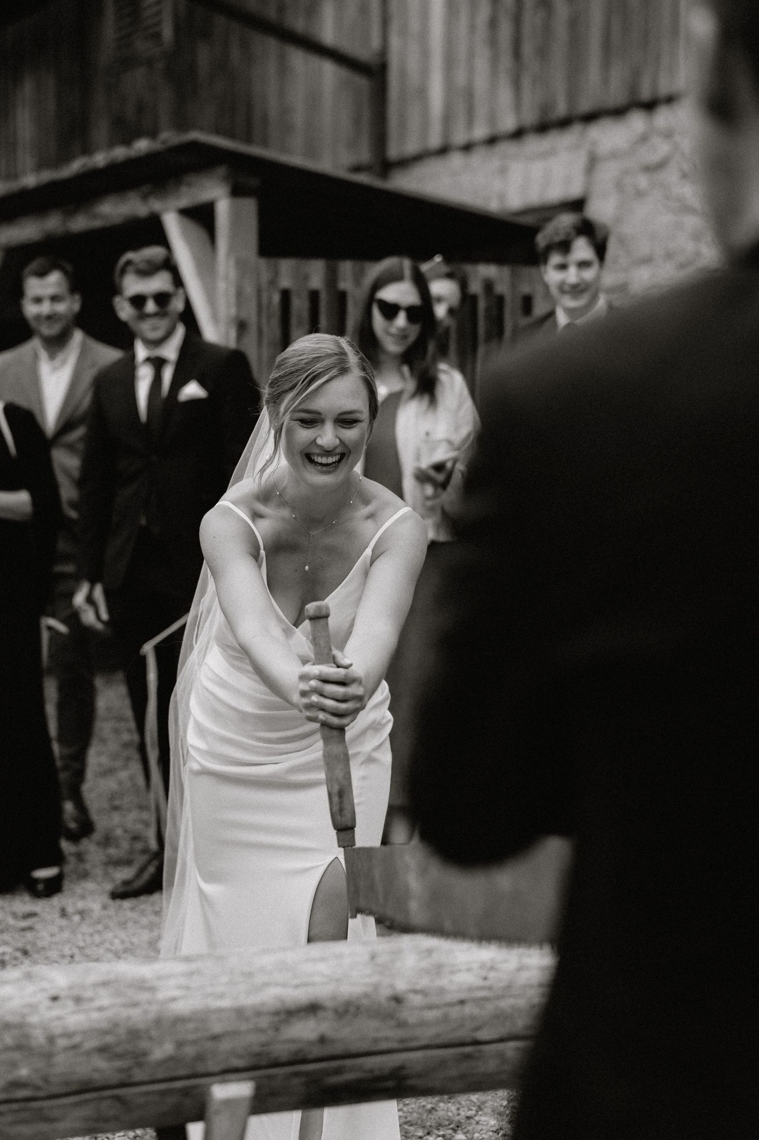 A person in a white dress participates in a traditional wedding log-sawing ceremony.