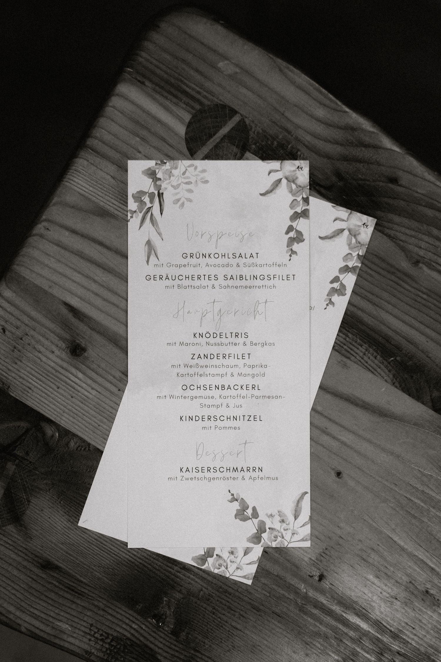 Black and white wedding menu cards with floral designs displayed on a wooden surface.