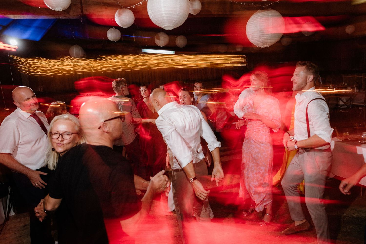 Wedding reception dance floor with red lighting effects and white paper lantern decorations.