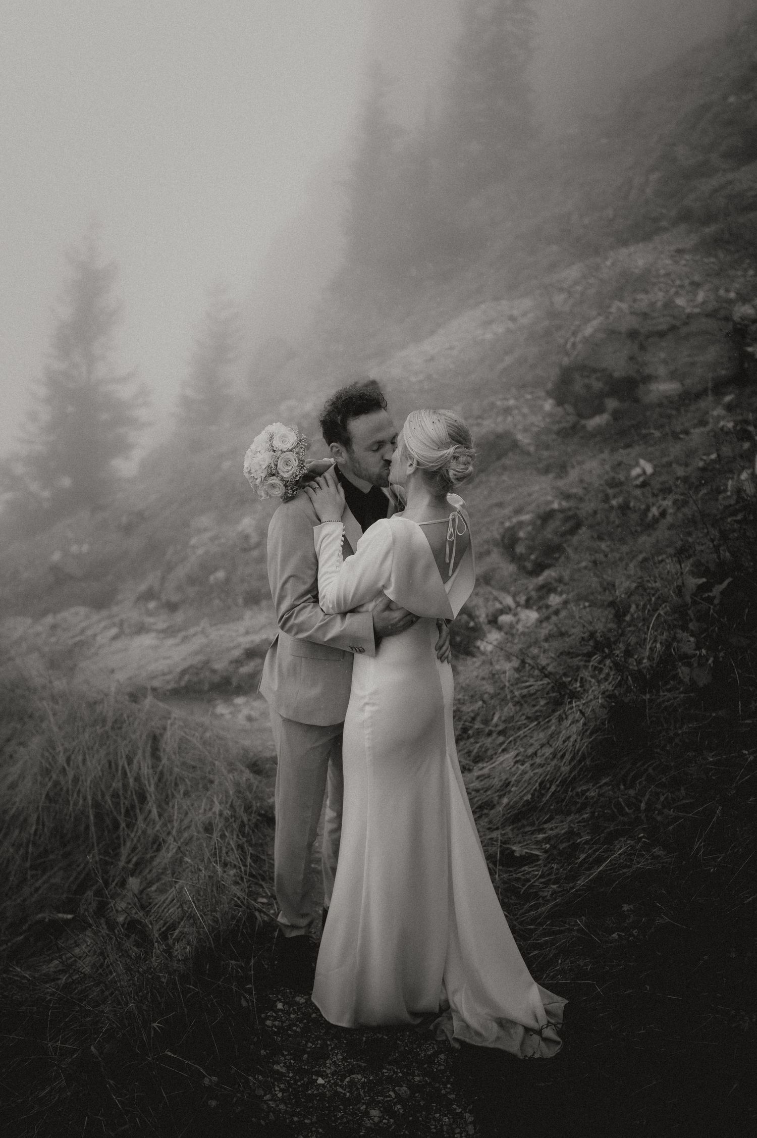Atmospheric black and white wedding photo with mountain fog in background.