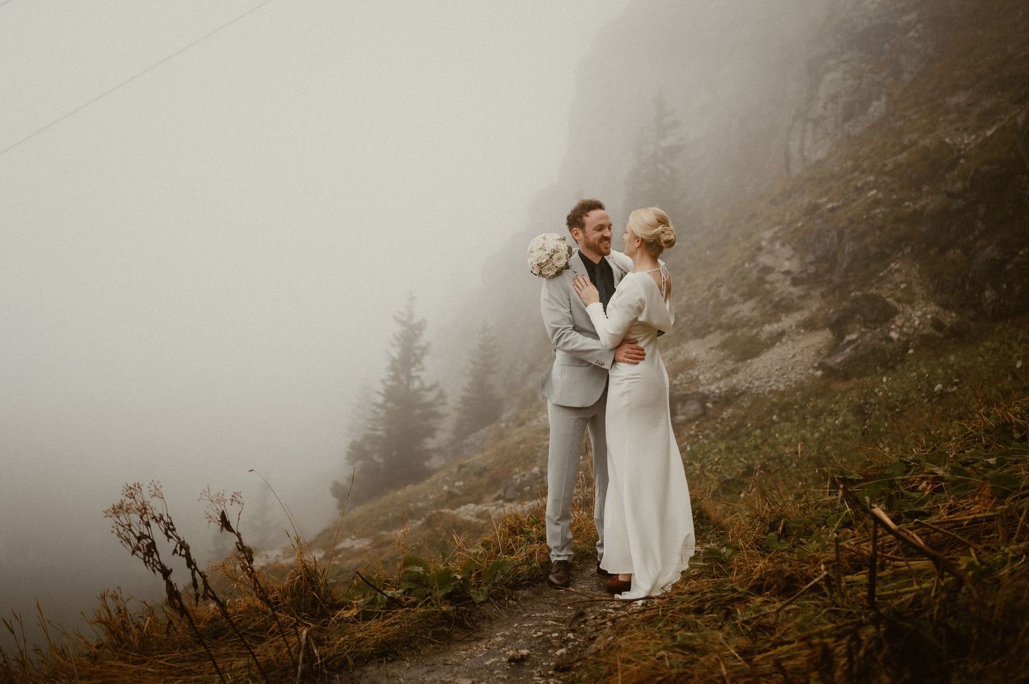 Wedding couple poses against a dramatic foggy mountain backdrop.