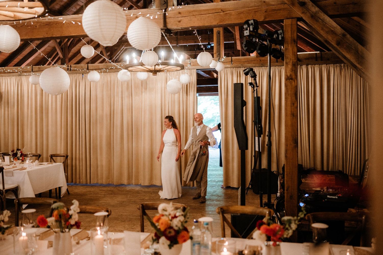 Wedding reception space with draped fabric, lanterns and romantic lighting in a rustic barn setting.