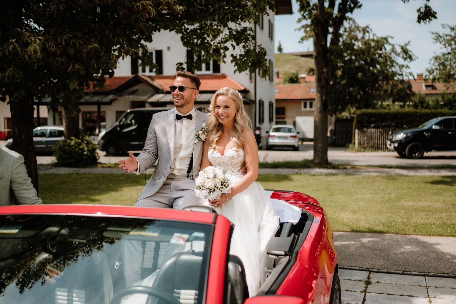A classic red convertible car parked on grass during a wedding celebration.