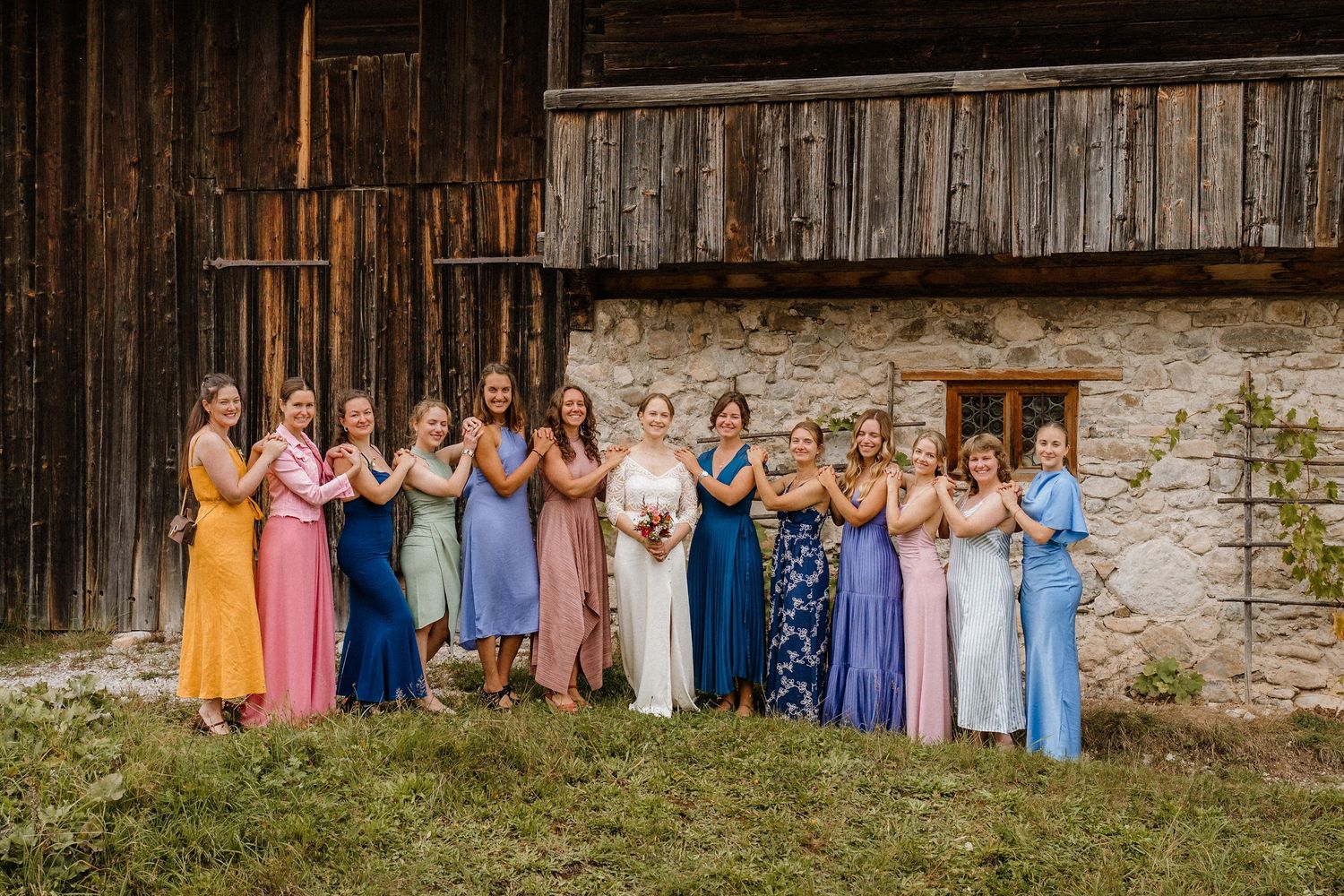 Wedding party in colorful attire posed in front of rustic wooden barn.