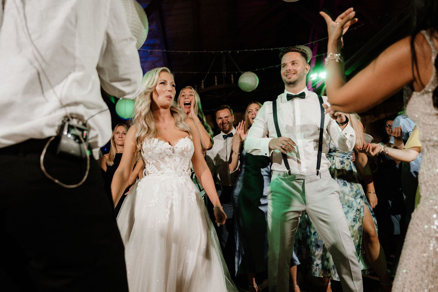 Wedding celebration in a rustic barn venue with guests dancing under white paper lanterns.