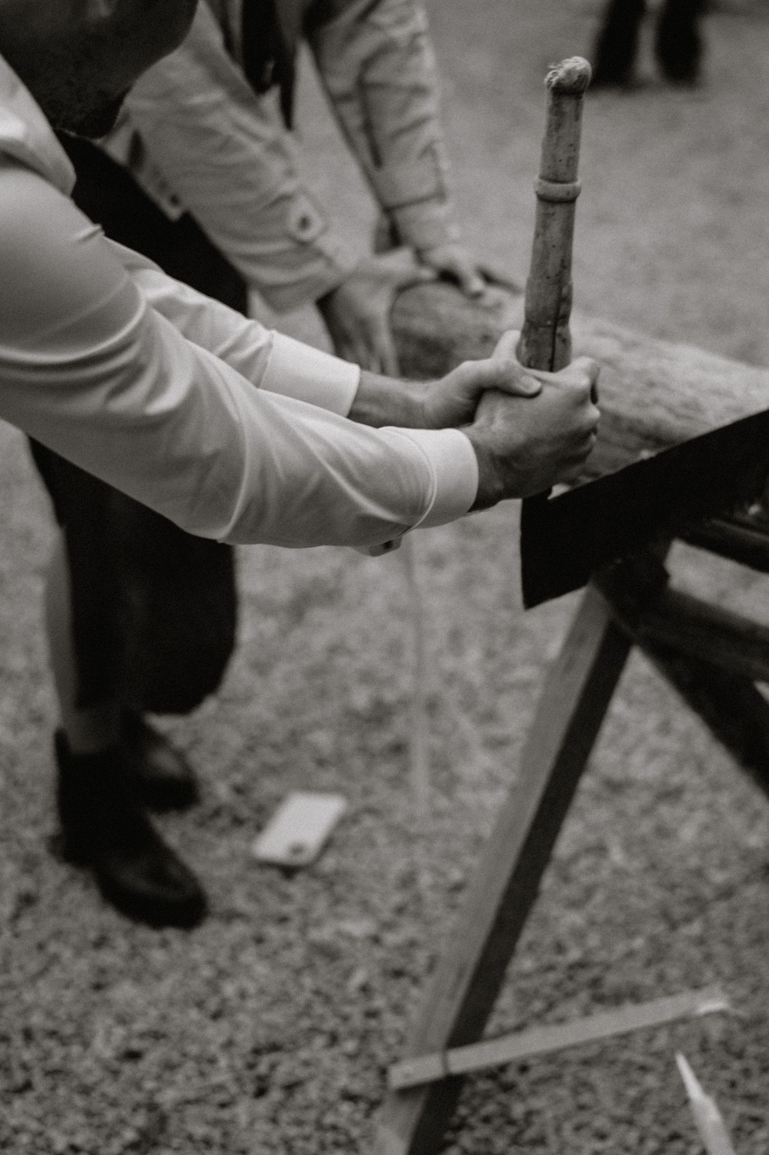 Close-up black and white shot of hands working on a traditional log-sawing task.