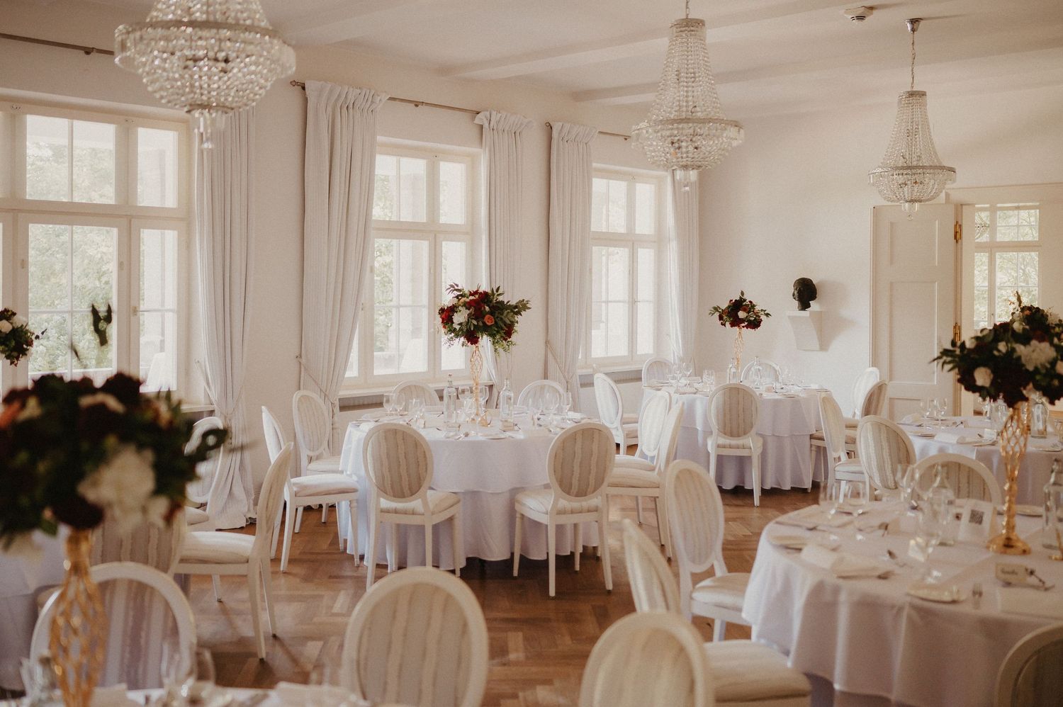 Bright white wedding reception hall with crystal chandeliers and classic French-style decor.
