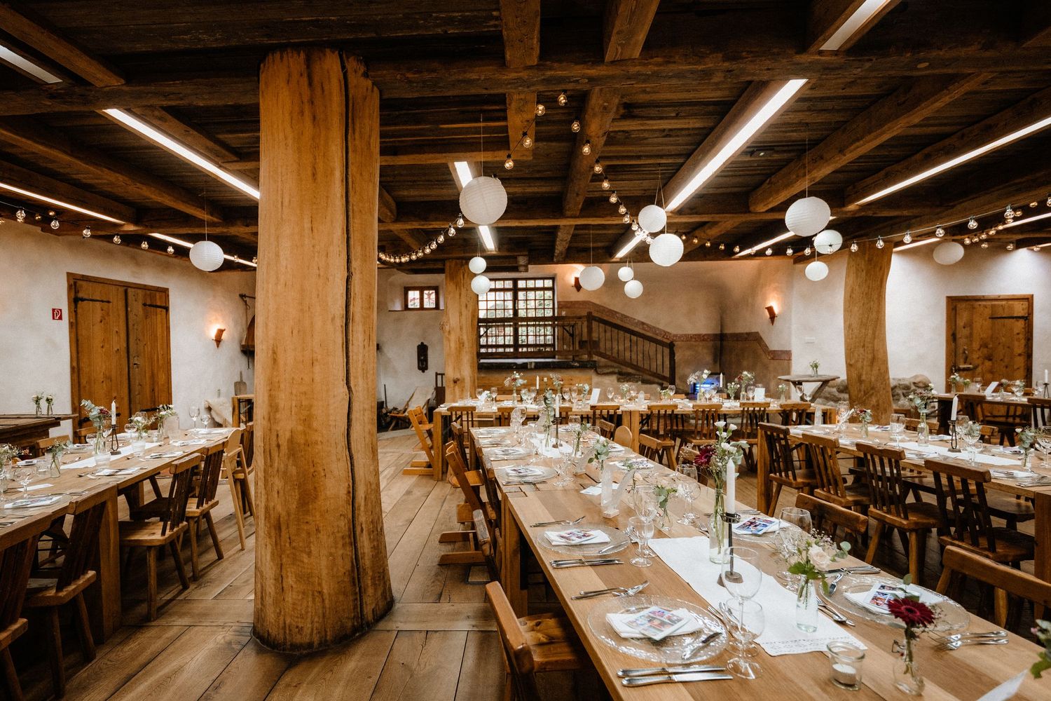 Large rustic reception hall with wooden beams and tables set for a wedding celebration.