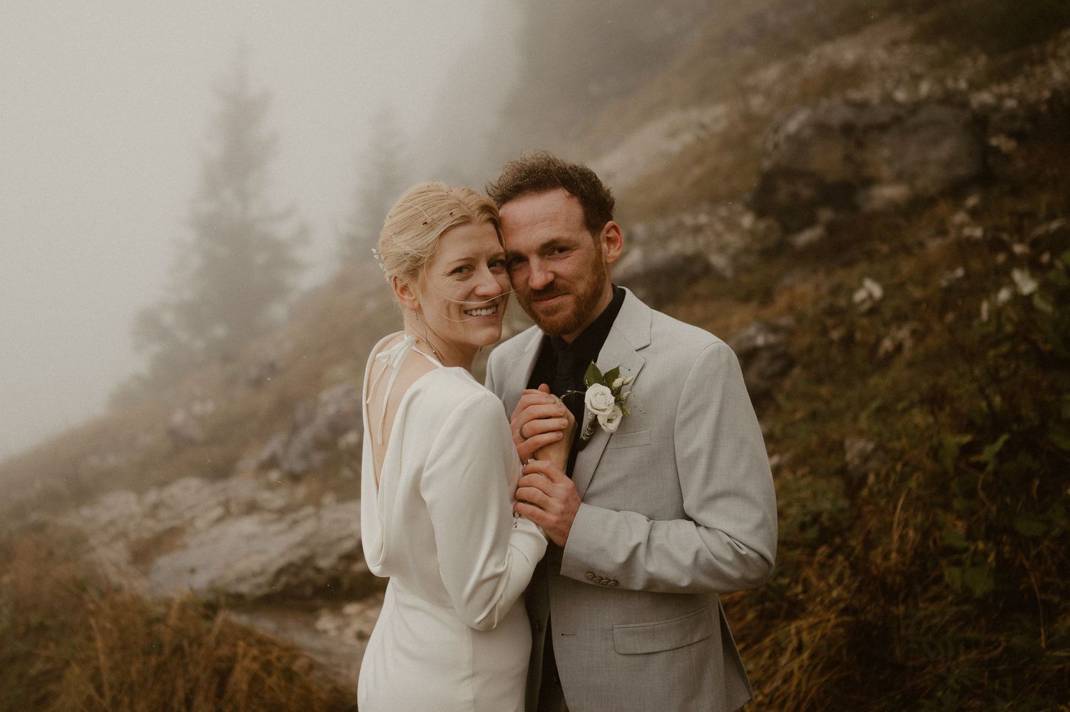 Intimate wedding portrait of couple in elegant attire against misty mountain backdrop.