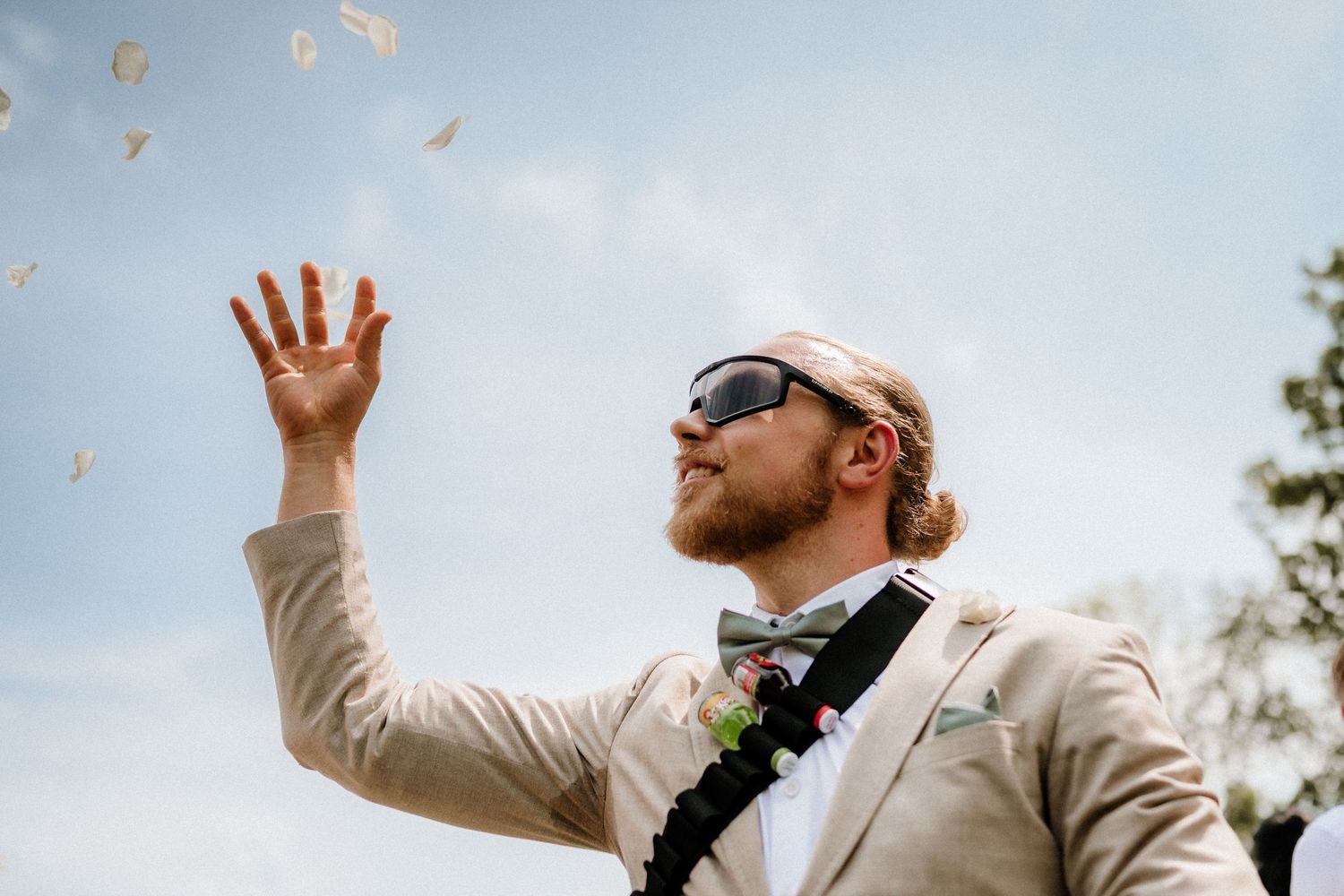 People reach up to catch something being tossed in the air at an outdoor wedding.