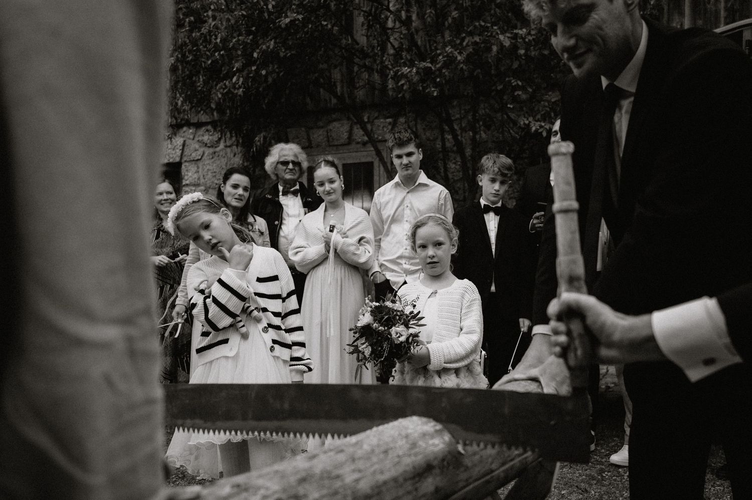 Black and white photo of wedding guests watching a traditional log sawing ritual.