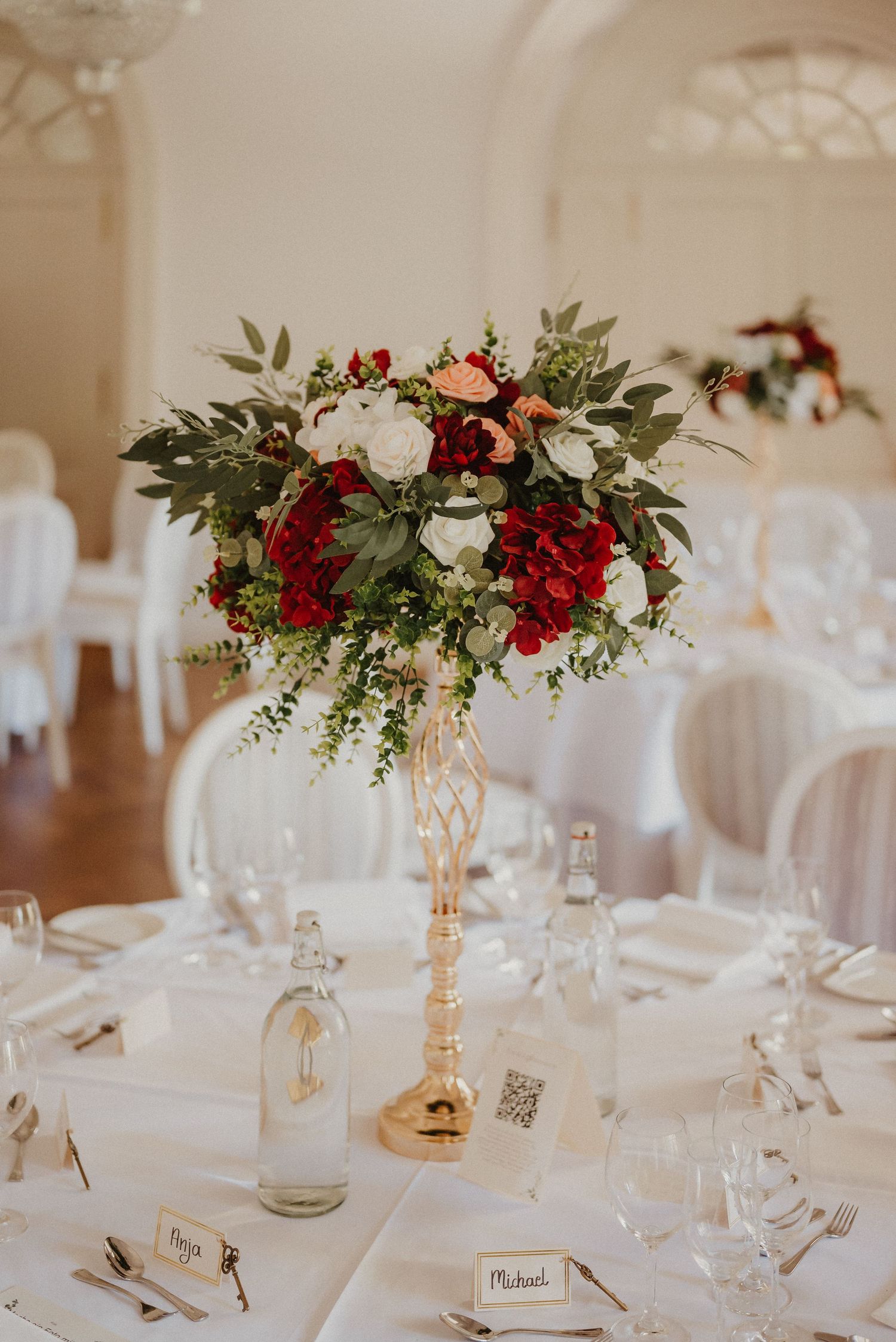 Wedding table settings with red and white floral centerpieces and gold accents.