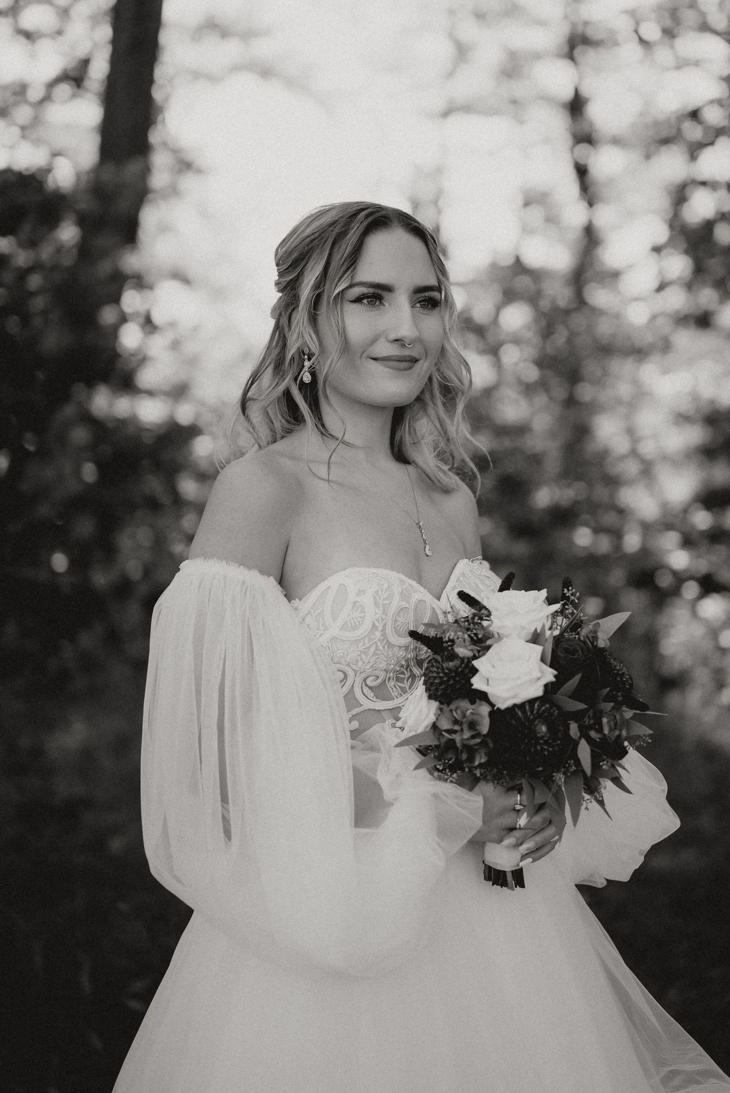 Elegant bridal portrait with off-shoulder white gown and bouquet in forest setting.
