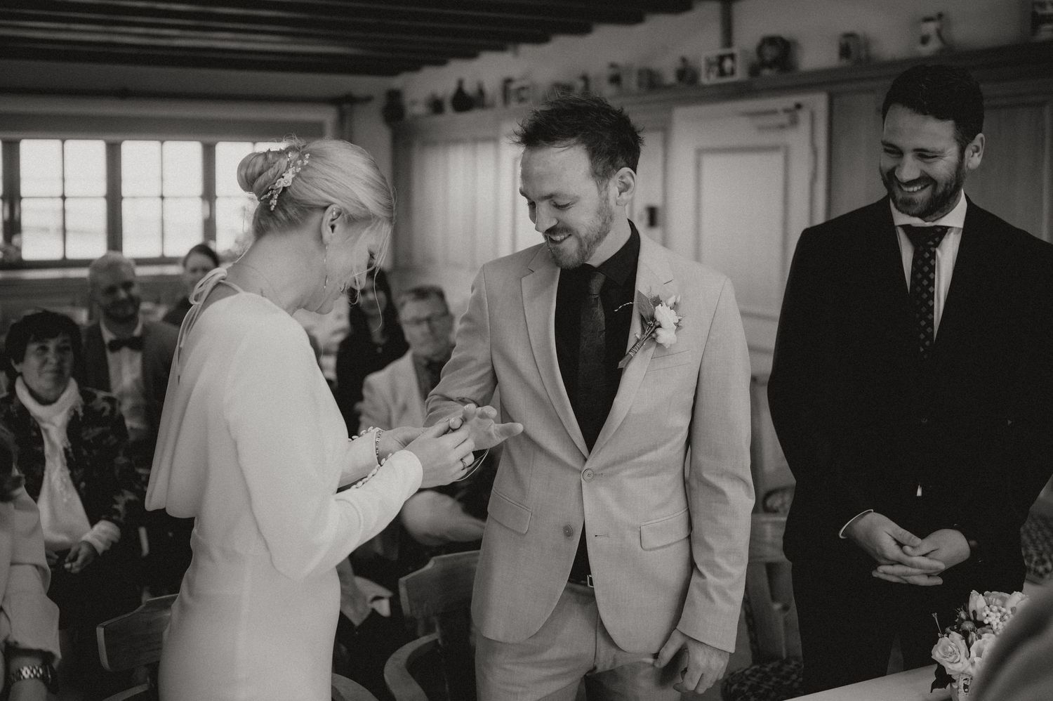A couple exchanges rings during an intimate indoor wedding ceremony with exposed wooden beams overhead.