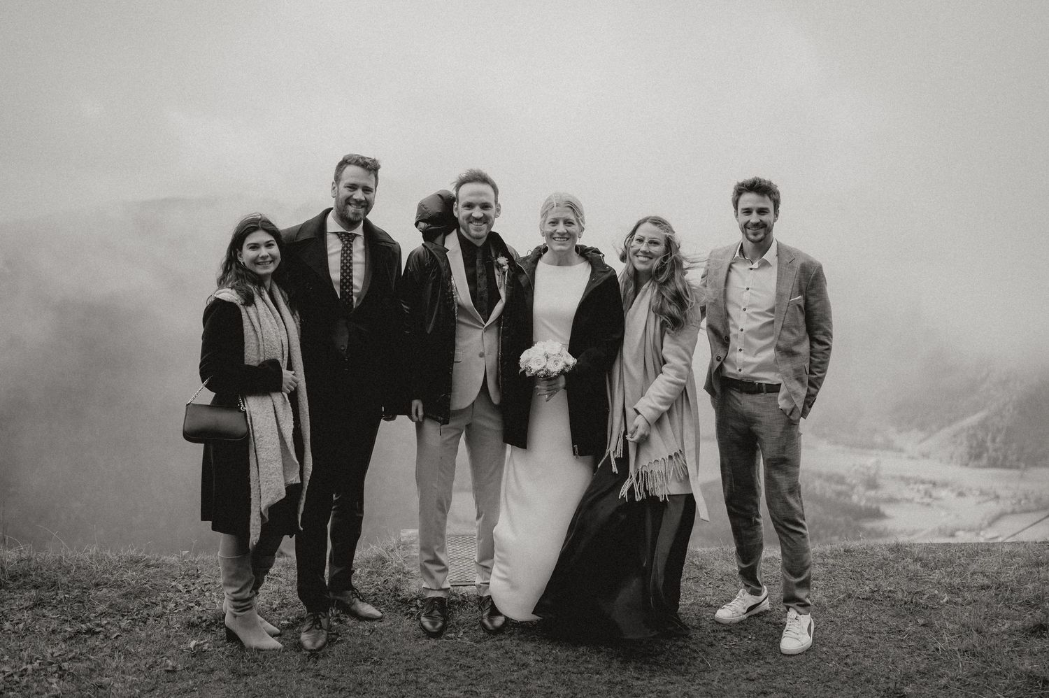 Group of wedding guests posing together on a misty mountain overlook.
