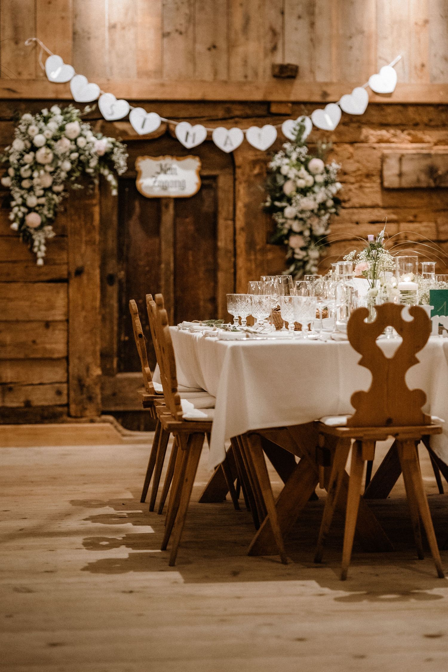 Rustic barn wedding reception tables decorated with white linens and floral arrangements under string lights.