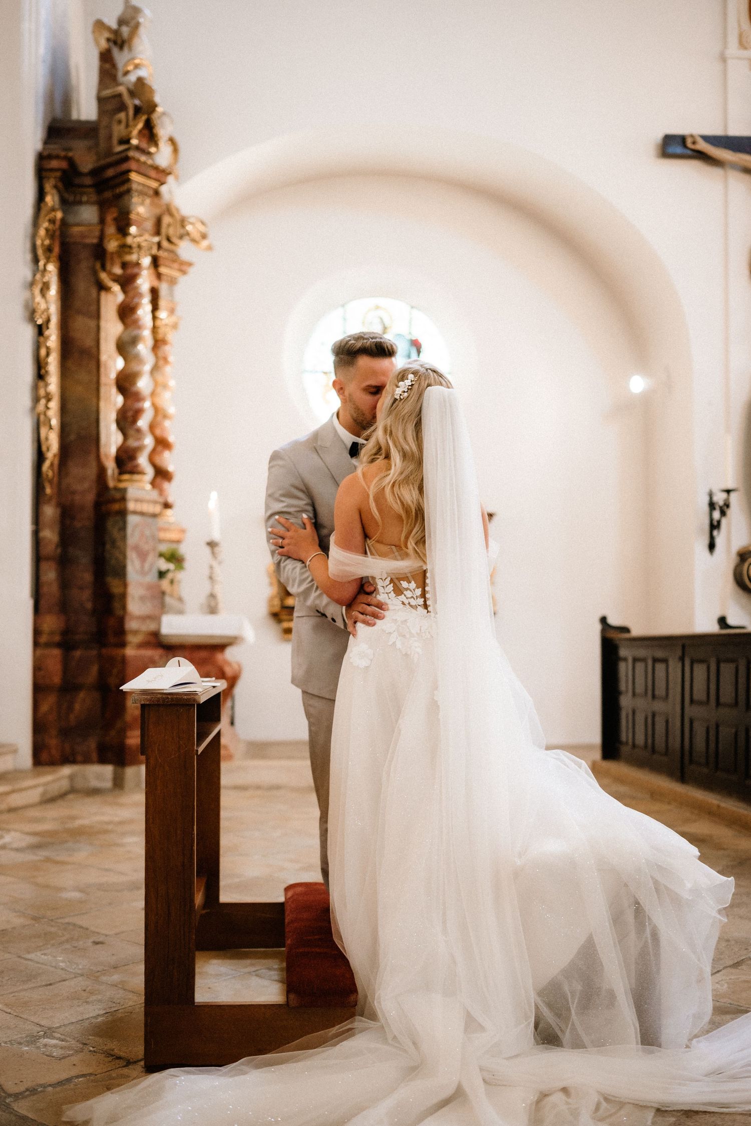Romantic wedding photos captured in the aisle of a traditional church with white walls and wooden details.