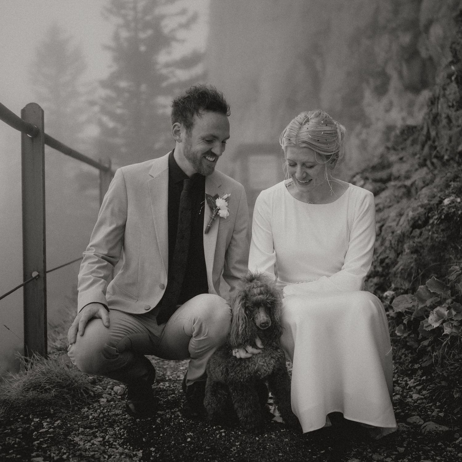 A couple shares laughter while sitting together on a misty mountainside.