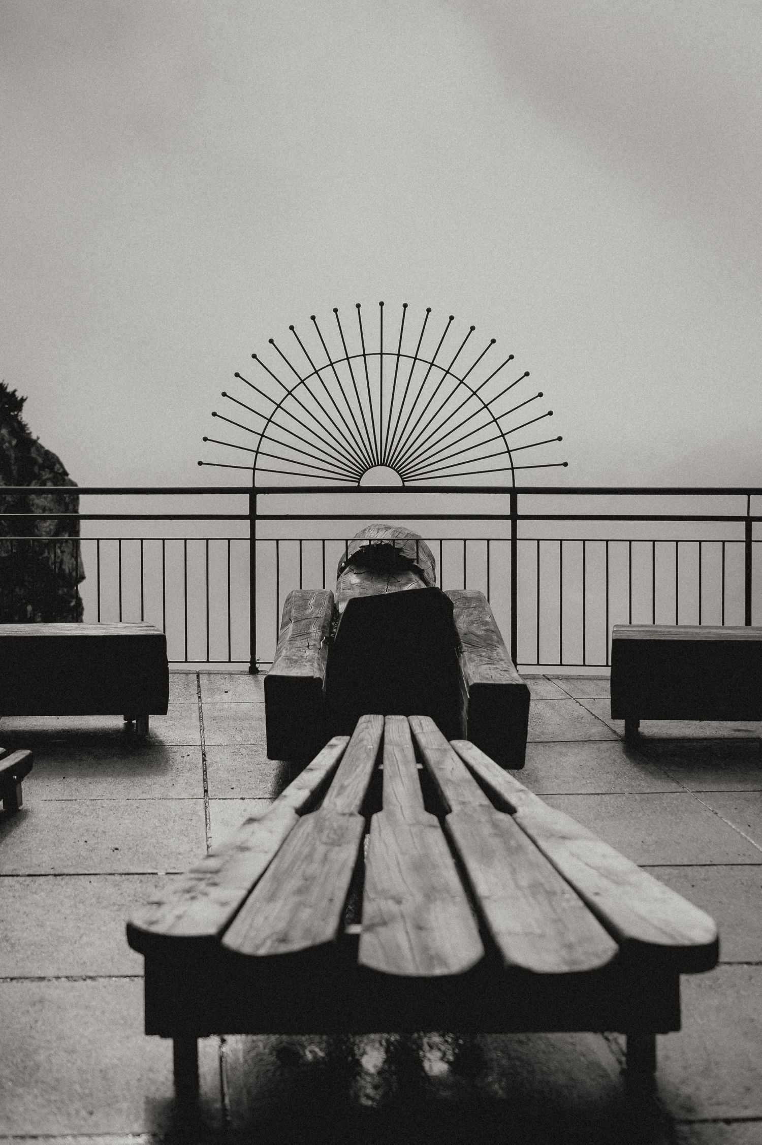 Minimalist black and white photo of benches with decorative sunburst railing design.
