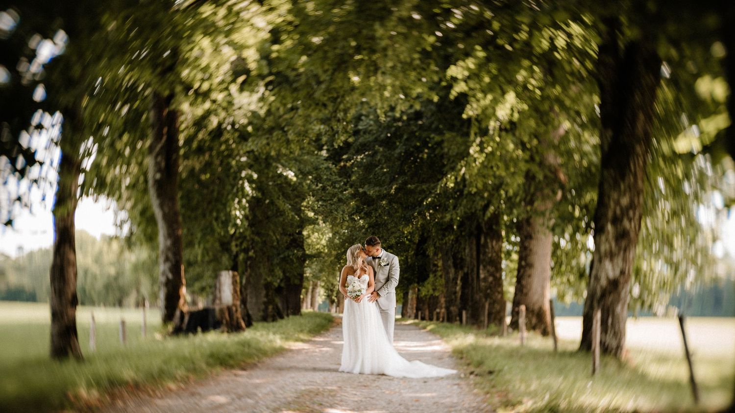 Der von Bäumen geseinte Weg schafft einen natürlichen Tunnel für romantische Hochzeitsfotografie. Von Dama Fotografie Bad Tölz
