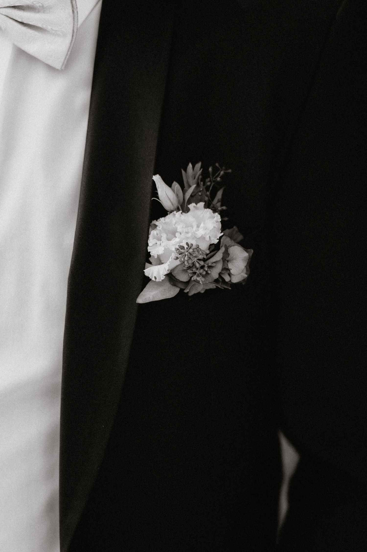 Close-up detail of white boutonniere flowers against dark formal suit.