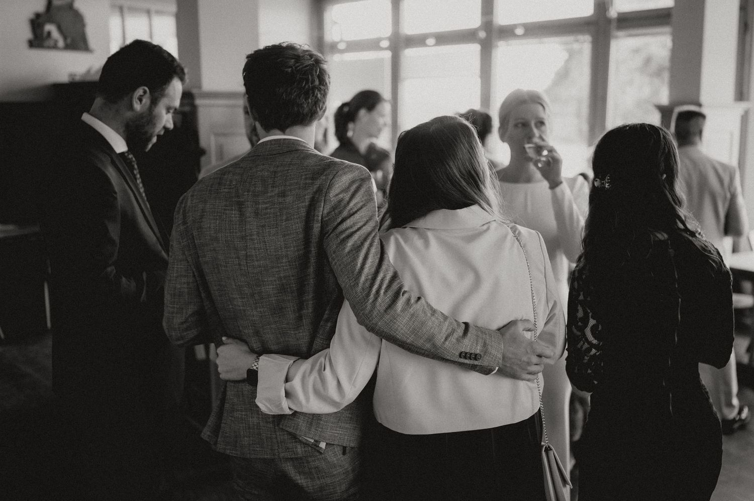 Wedding guests gather in groups for conversations during an indoor reception.