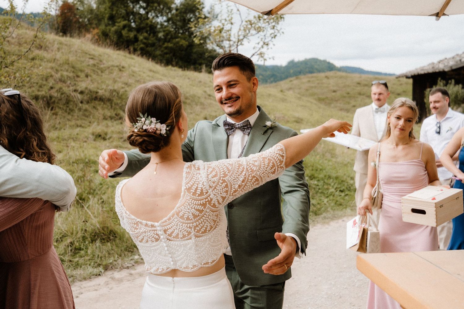 Wedding guests mingle and celebrate under white umbrellas in an outdoor mountain setting.