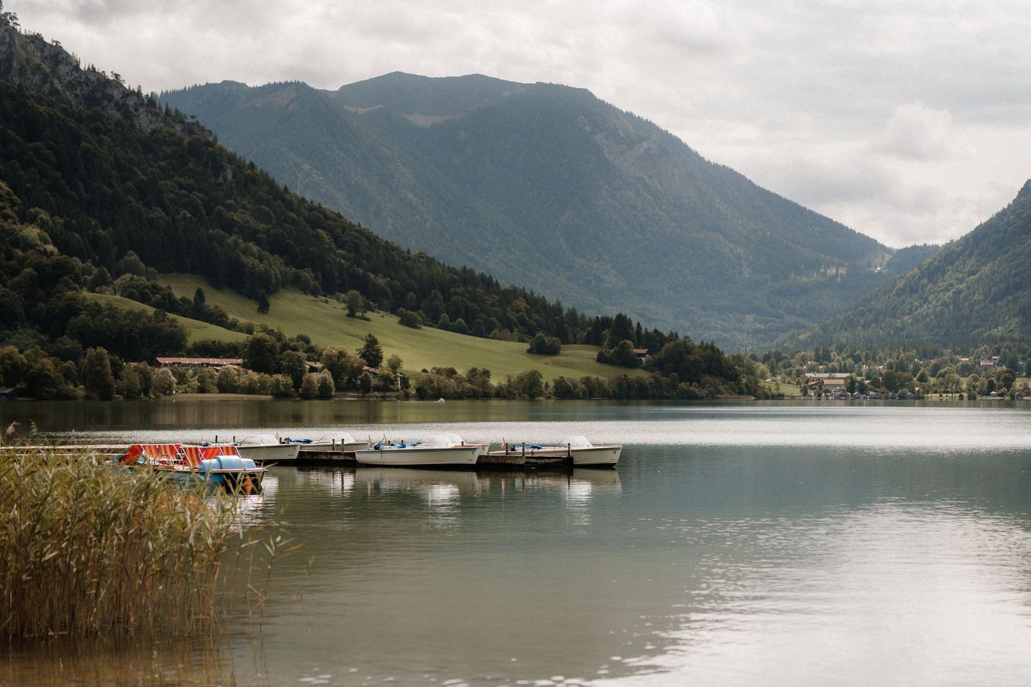 Serene mountain lake view with boats and docks under overcast sky.