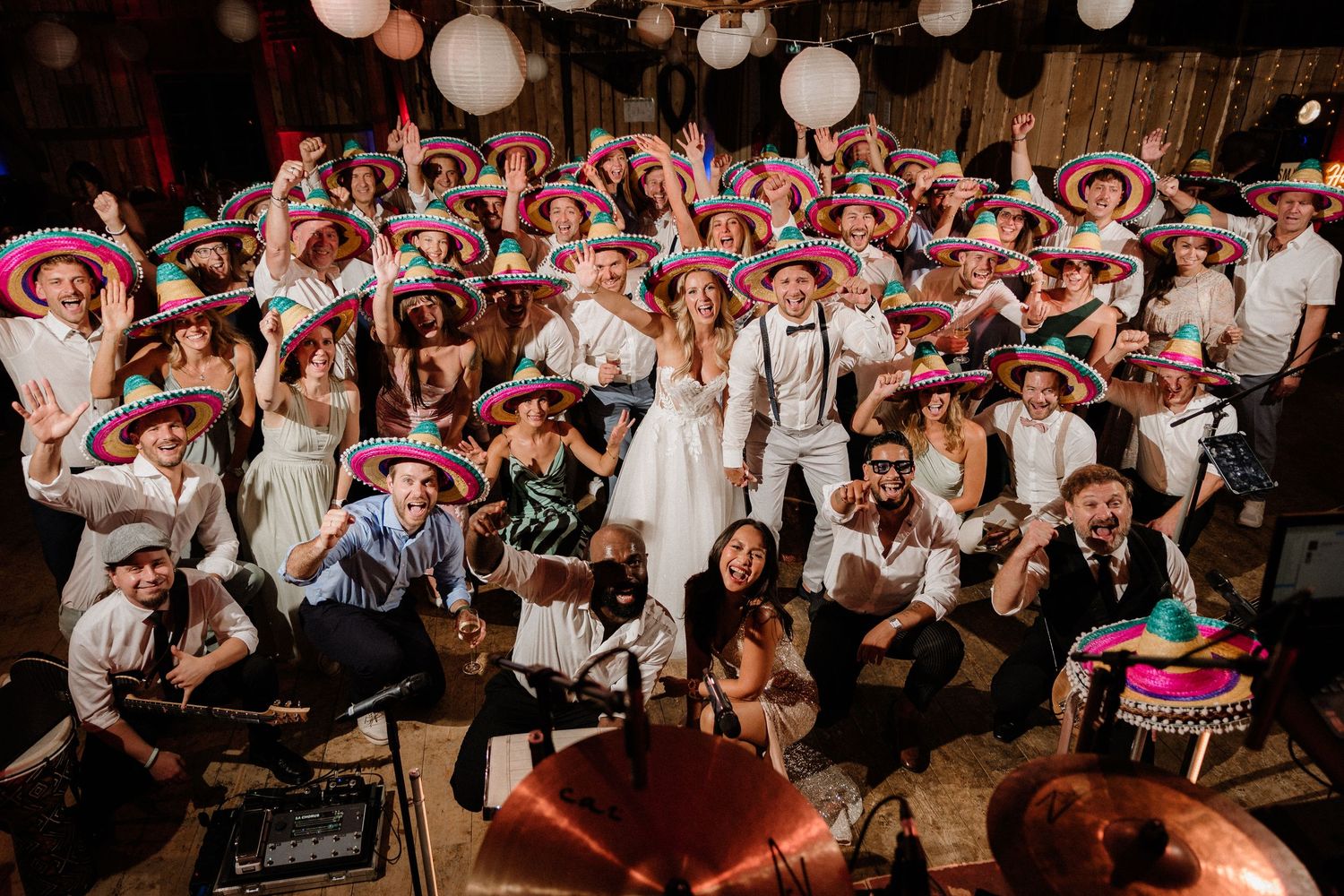 Large group photo of wedding guests wearing matching colorful Mexican sombreros.