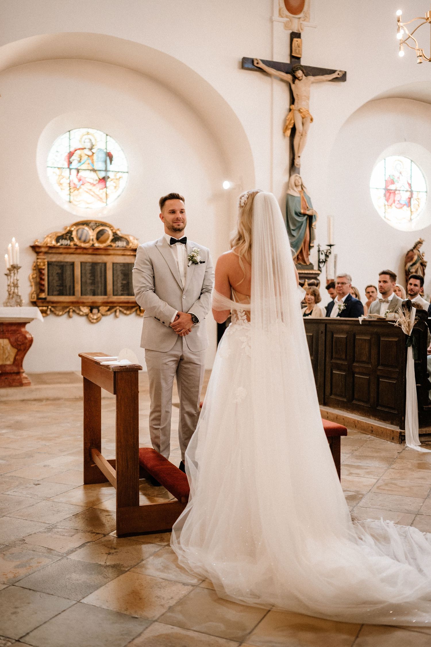 Wedding ceremony in a traditional church with ornate wooden pews and religious decor.