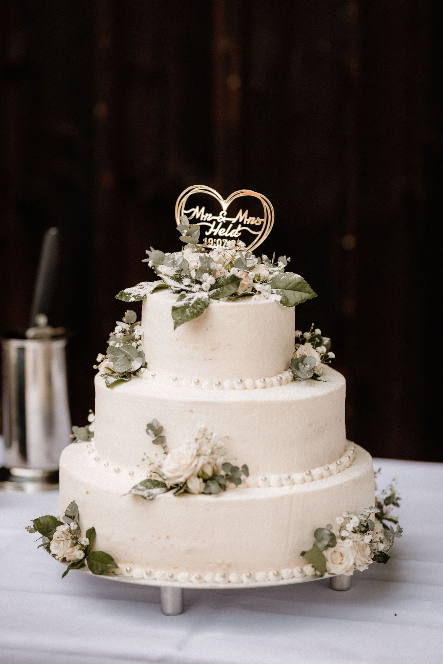Three-tiered white wedding cake decorated with delicate flowers and a heart topper.