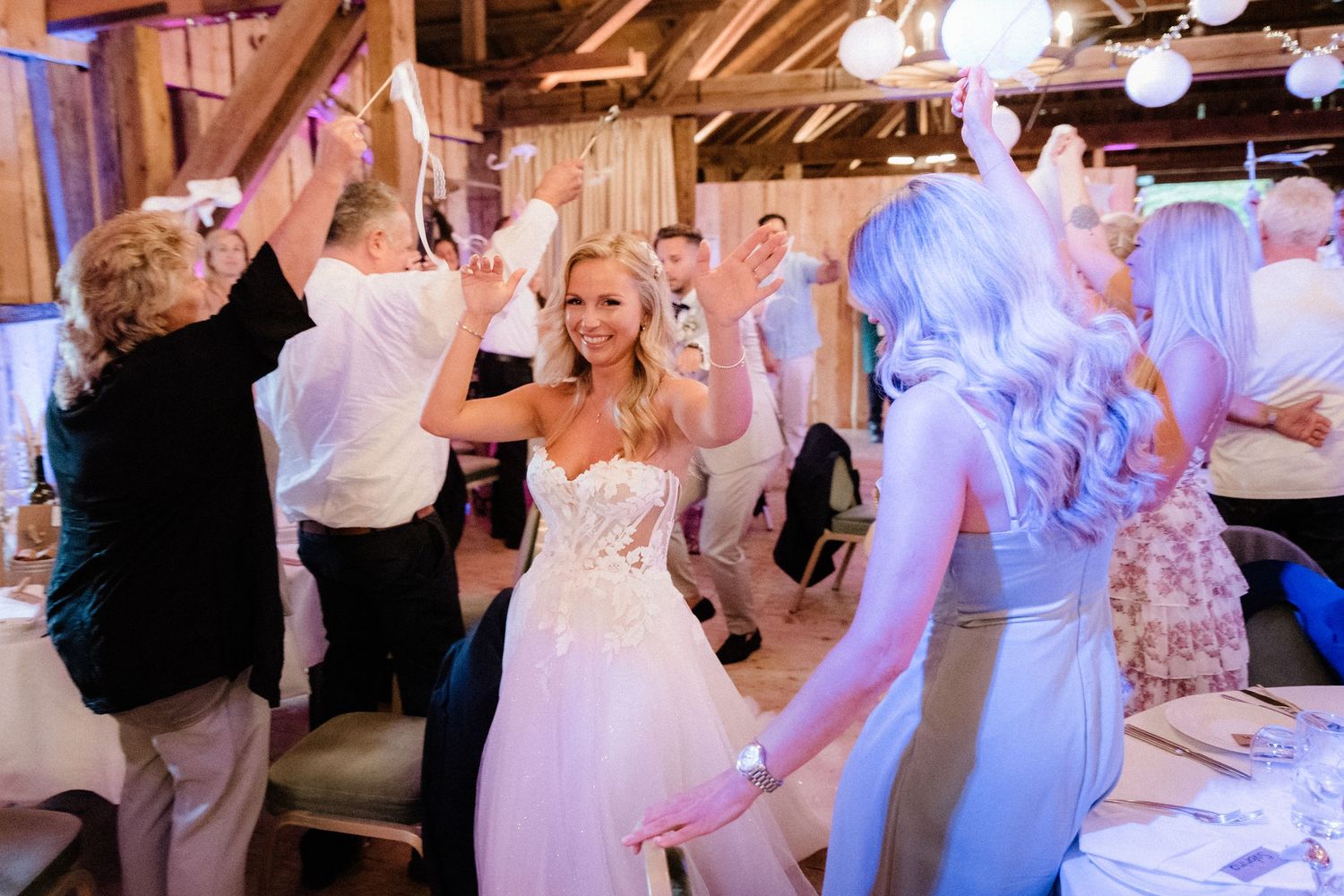 Wedding guests dancing under purple lighting in rustic barn reception venue.