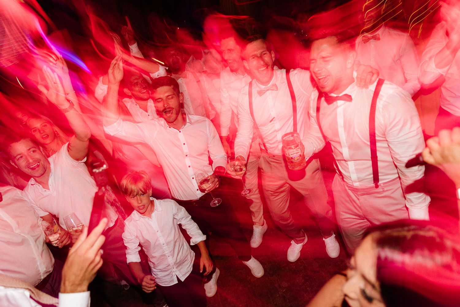 Wedding party dancing under dramatic red lighting at a reception celebration.