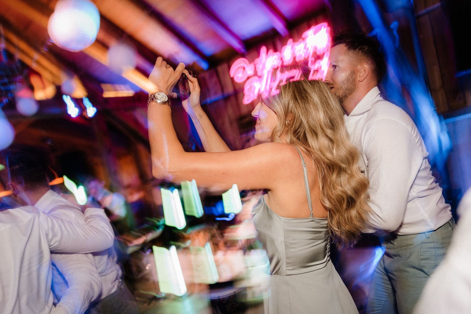 Dance floor filled with party guests illuminated by vibrant blue and pink lighting.
