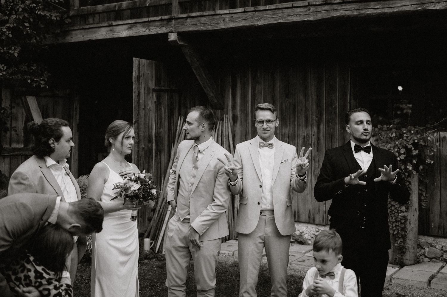 Wedding party members in light colored attire pose together for group photos outside a rustic barn venue.
