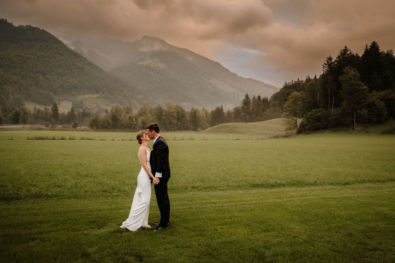 Panoramic view of a couple in a vast meadow with mountains in the background.