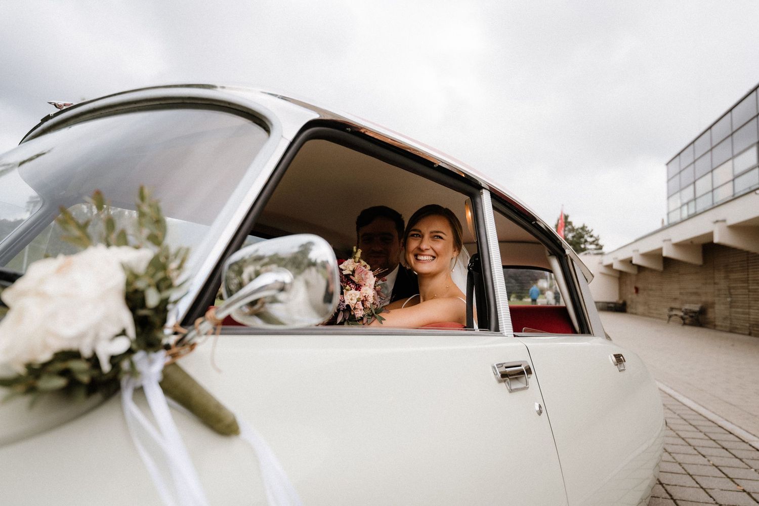 Elegant wedding couple poses with classic white Citroen DS car.