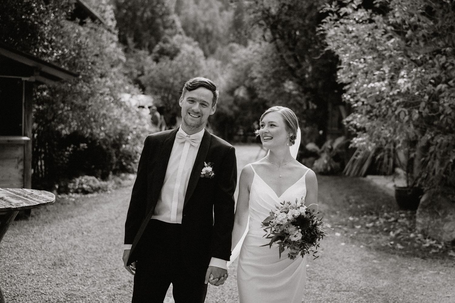 Black and white wedding portrait on garden path with rustic backdrop.