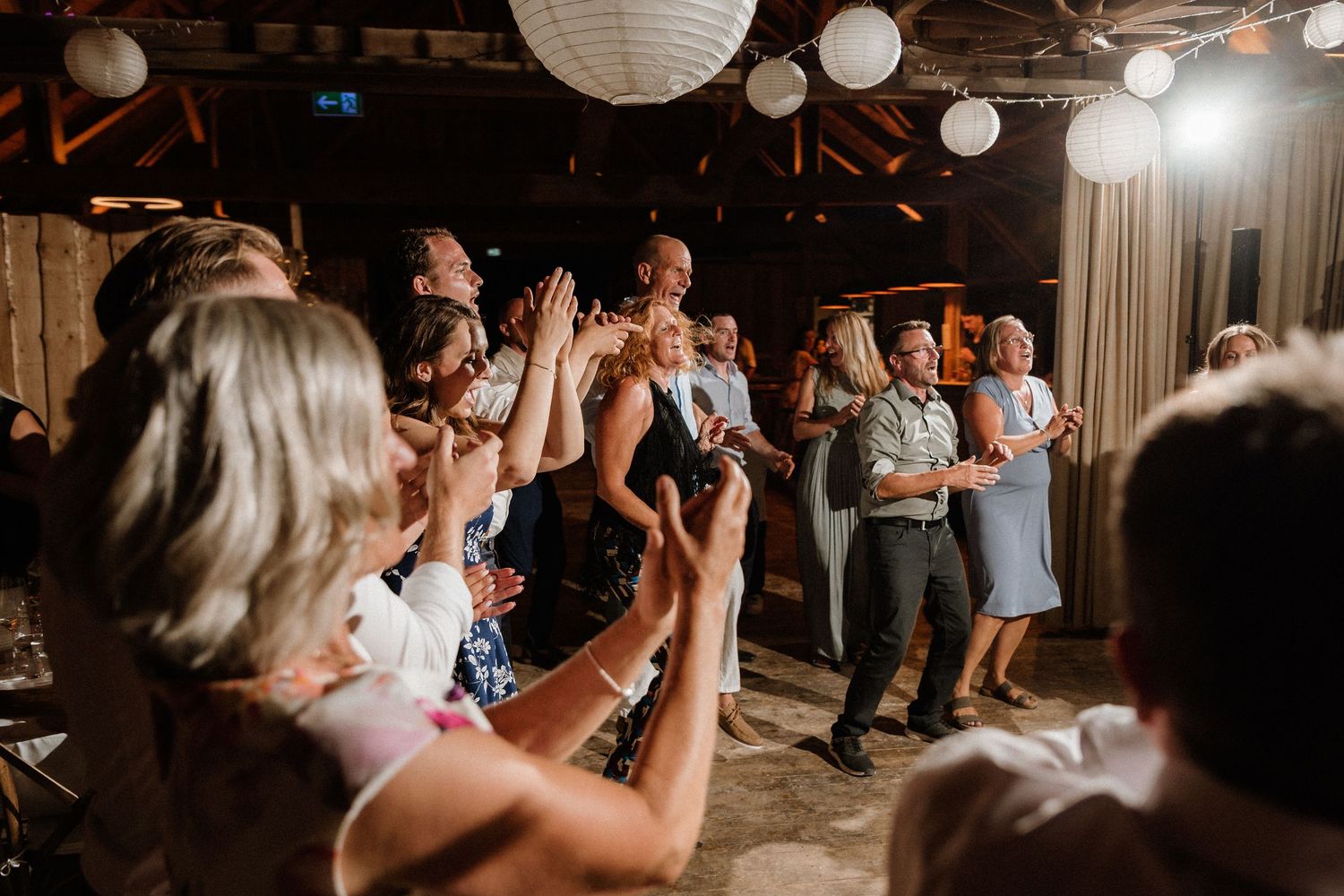 Dance floor filled with wedding guests under white paper lanterns and warm lighting.
