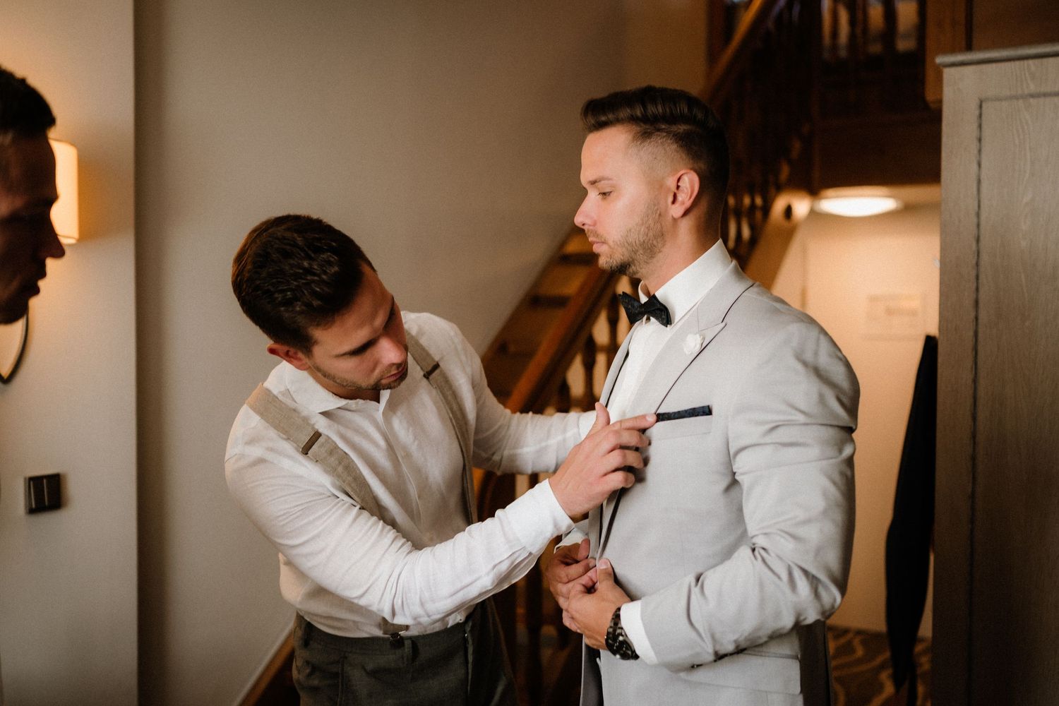 Wedding preparation scene showing formal attire adjustments in warm lighting.