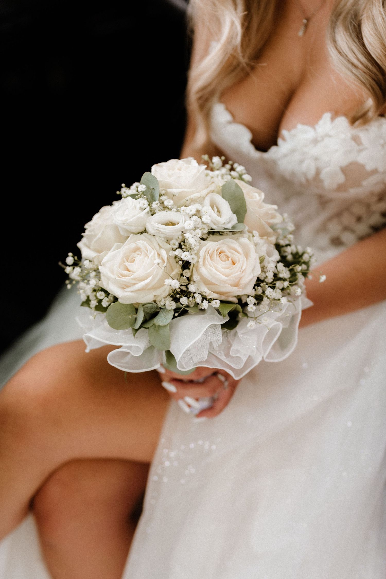 Nahaufnahme von zarten weißen Rosen- und Baby-Atem-Corsagen mit Perlenakzenten an den Handgelenken bei einer Hochzeitszeremonie. Dama Foto