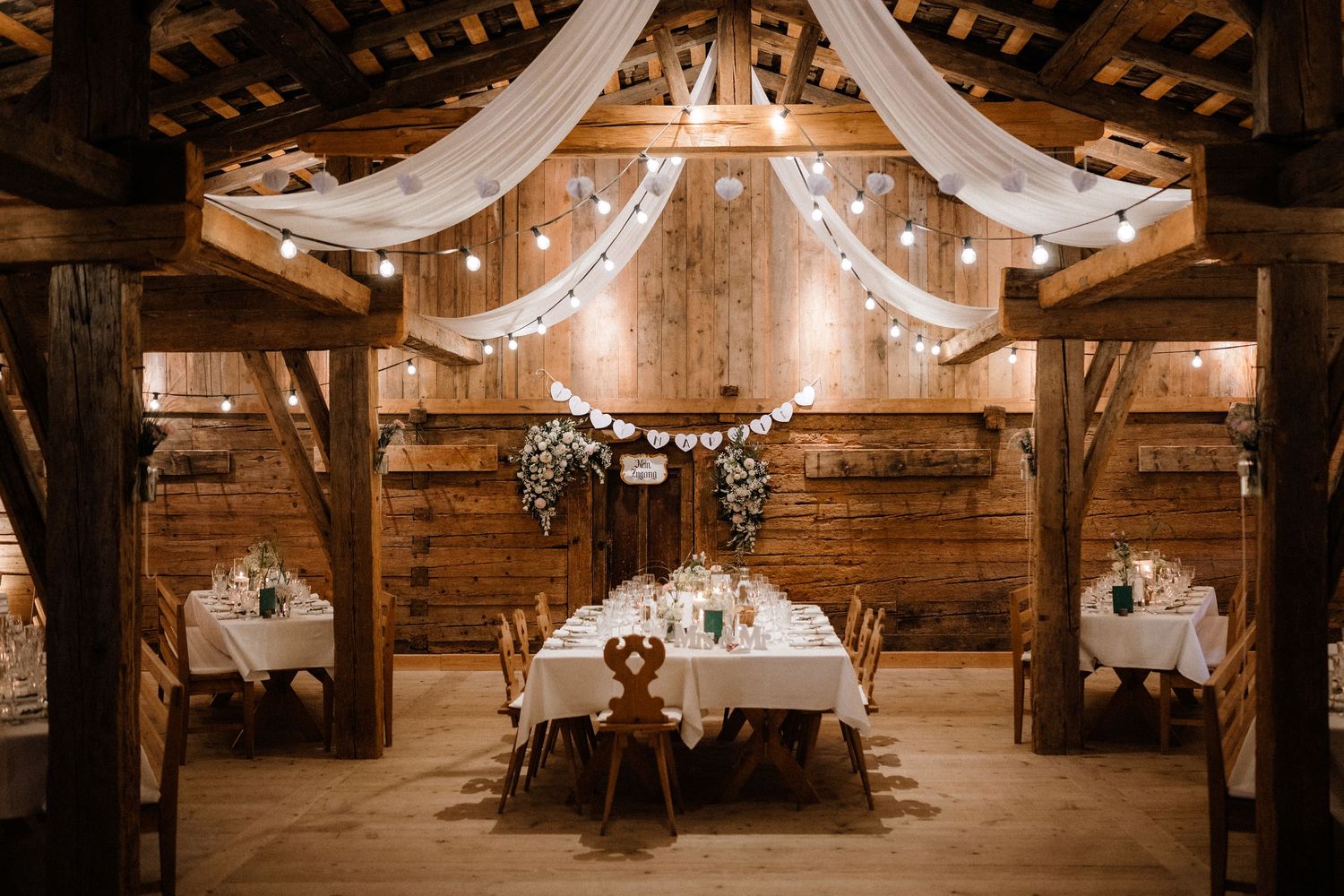 Elegant white fabric draping and string lights decorating the ceiling of a rustic wooden barn venue.